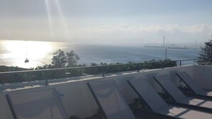 A rooftop terrace with sun loungers overlooking a body of water and distant industrial structures. - Milazzo INN AiMori (Milazzo)