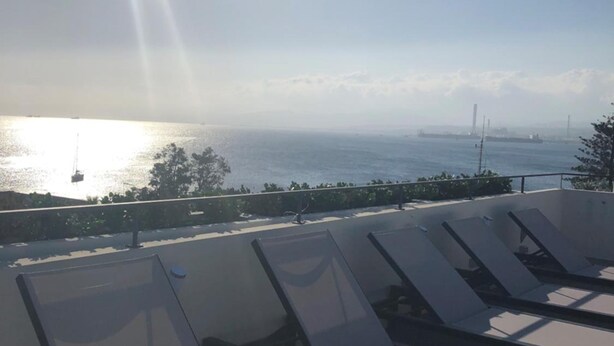 A rooftop terrace with sun loungers overlooking a body of water and distant industrial structures. - Milazzo INN AiMori (Milazzo)