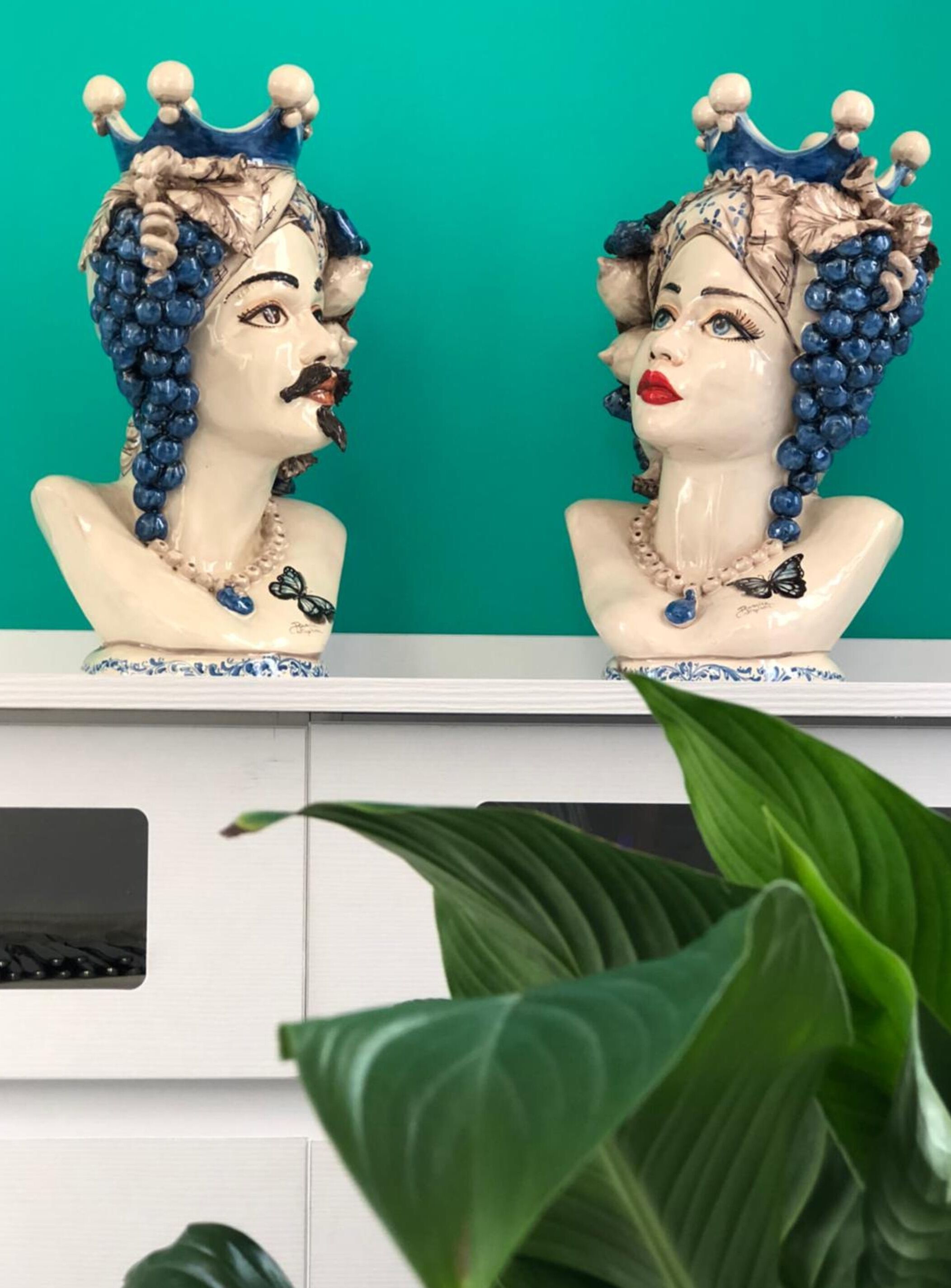 Two ceramic busts with crowns and jewelry against a teal background.