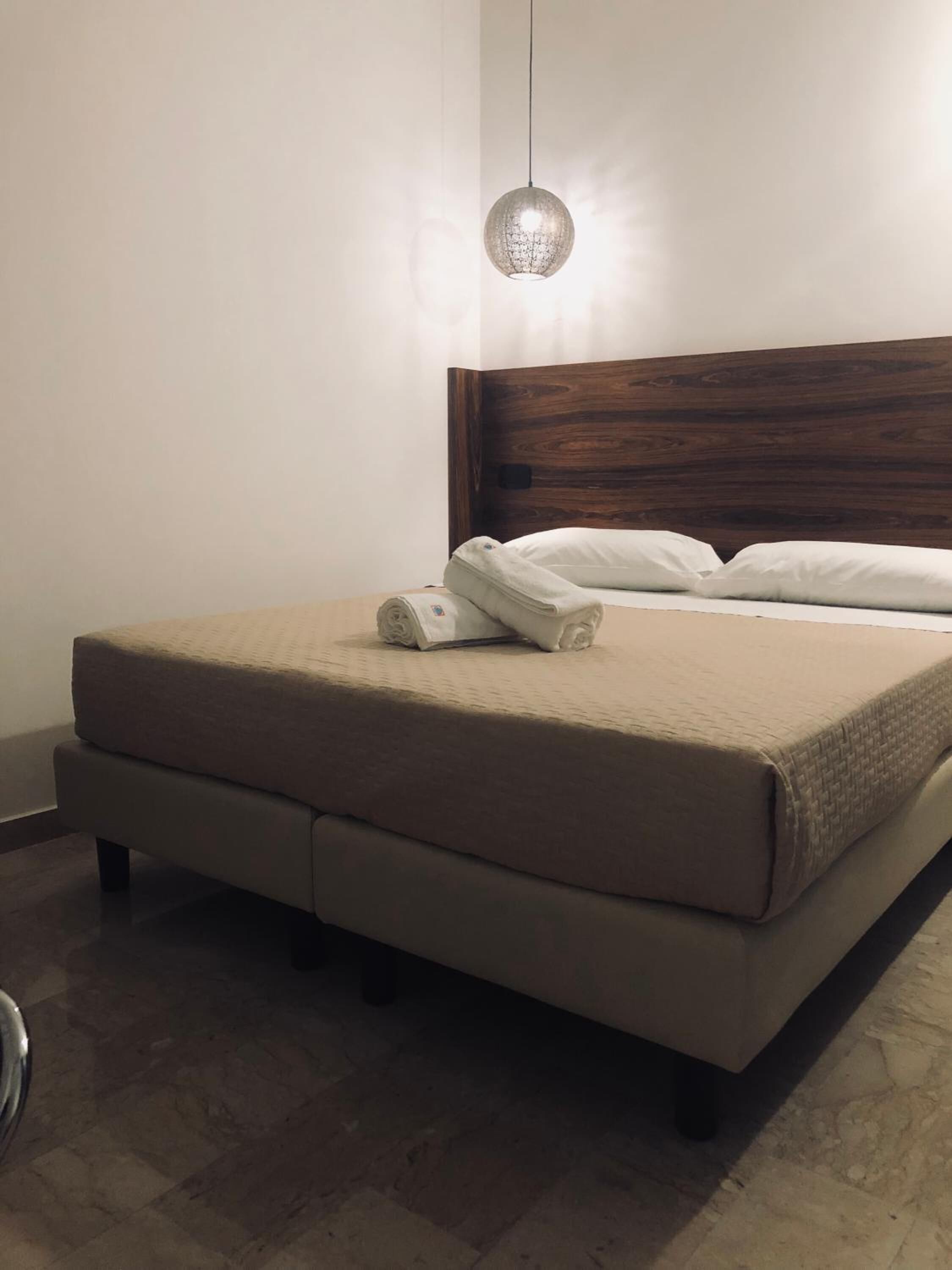 Una cama bien hecha con cabecera de madera, una lámpara colgante y un suelo con textura.