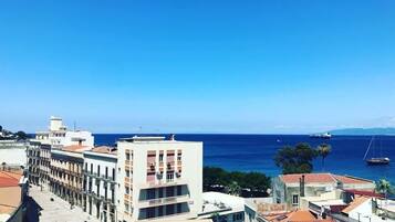 A coastal cityscape with a prominent building featuring a red roof and a balcony, overlooking the sea.