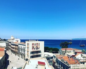 A coastal cityscape with a prominent building featuring a red roof and a balcony, overlooking the sea.