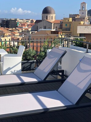 A rooftop terrace with lounge chairs and potted plants, overlooking a cityscape with historic buildings and a dome structure.