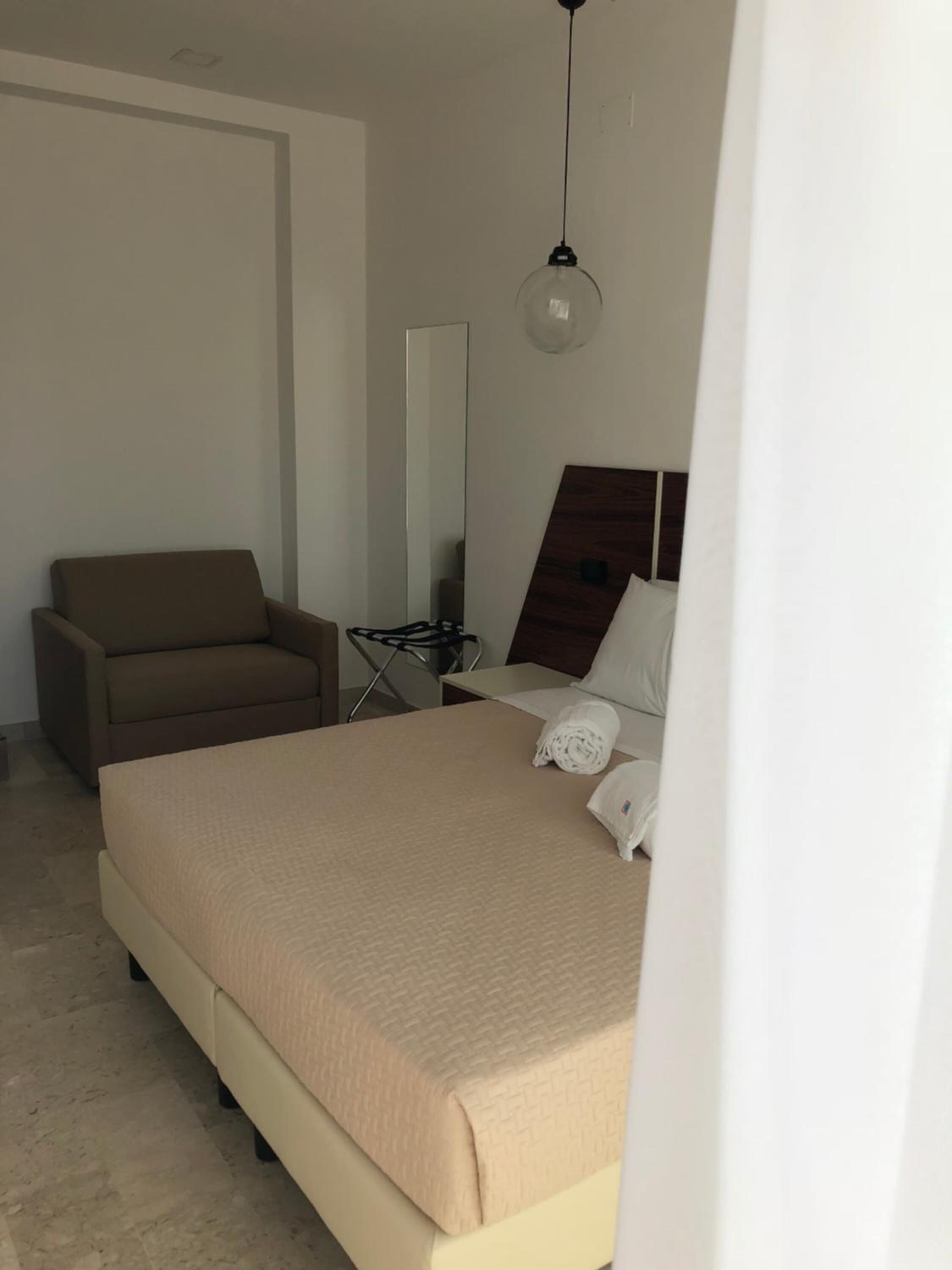 Una habitación de hotel con cama, una silla, escritorio, espejo y lámpara colgante.