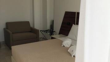 Una habitación de hotel con cama, una silla, escritorio, espejo y lámpara colgante.