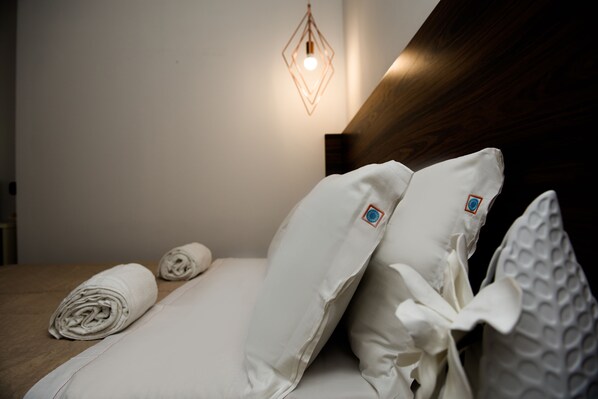 A neatly made bed with white linens and pillows, a wooden headboard, and a geometric light fixture on the wall.