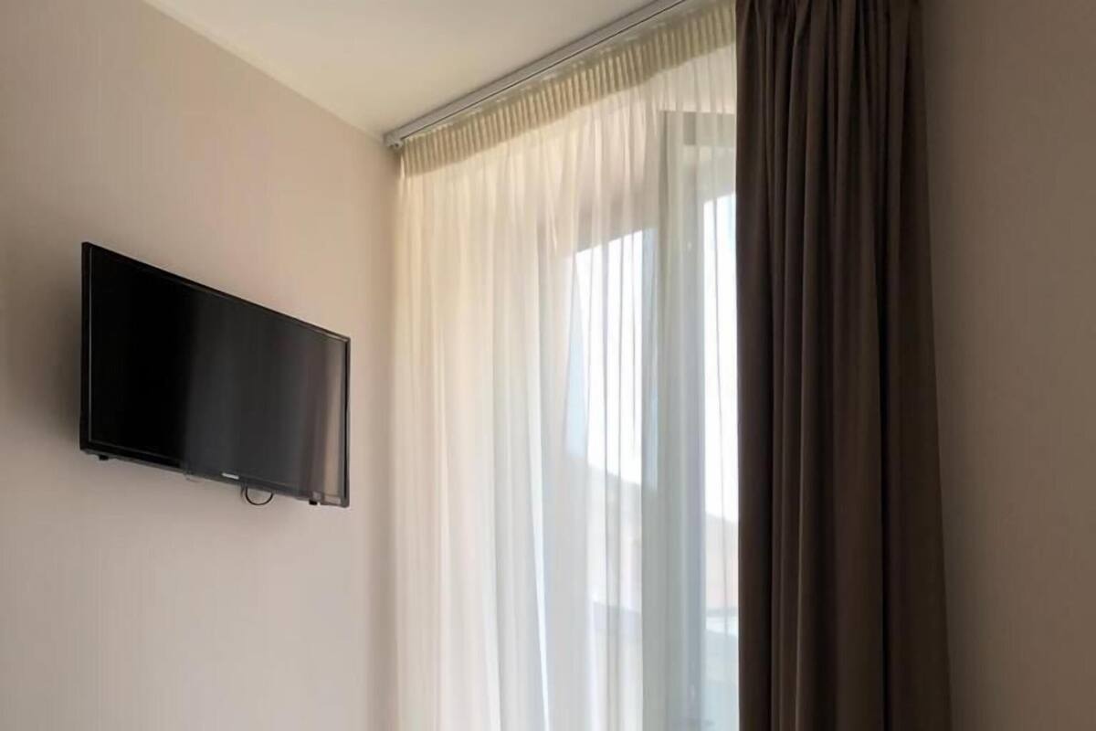 A hotel room with a bed, a TV mounted on the wall, and a window with curtains.