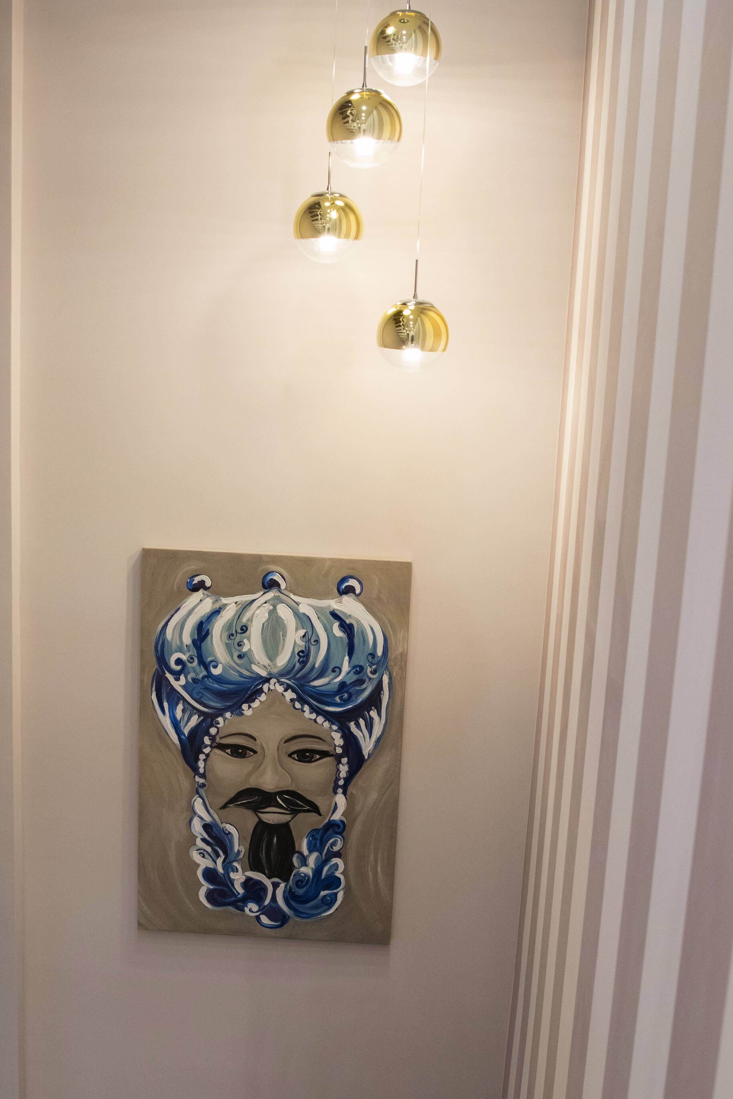 A hallway with a wall-mounted painting of a figure in traditional attire and four hanging spherical light fixtures.