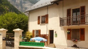Un edificio a due piani con un balcone, persiane in legno e un muro in pietra.