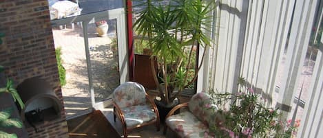 A sunlit patio with a brick wall, a glass door leading outside, a sofa, two chairs, a small table, and a potted plant.