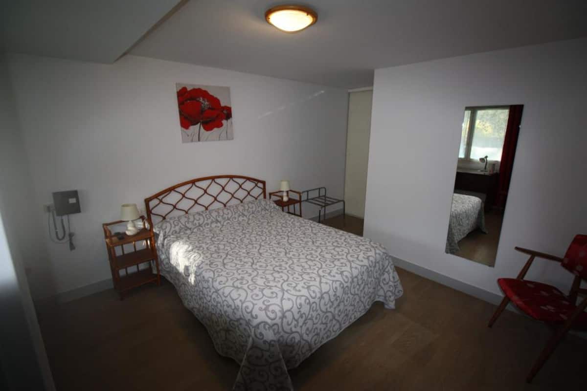 Un dormitorio con cama, mesitas de noche, un espejo y una silla roja.