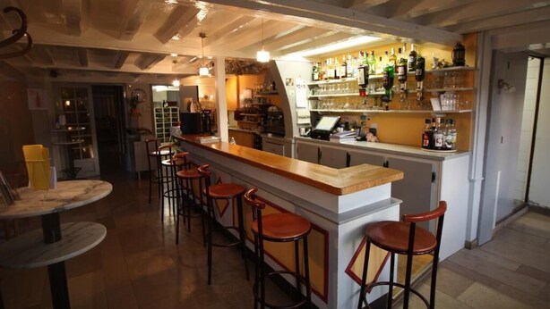 Un espace bar doté d’un long comptoir, de nombreux tabourets et d’étagères remplies de bouteilles.