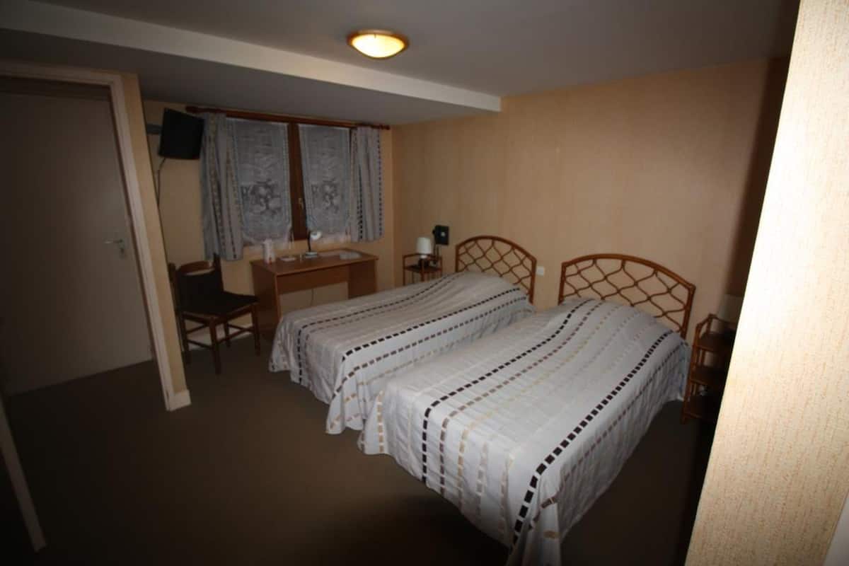 Un dormitorio con dos camas, un escritorio, una silla y un televisor en la pared.