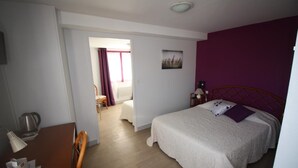 Une chambre d’hôtel avec un lit, un bureau doté d’une lampe, une chaise, une fenêtre avec des rideaux et un tableau accroché au mur.