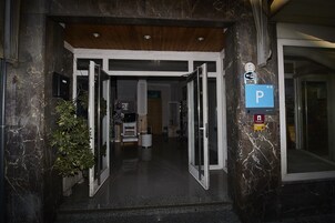 Entrada de hotel con fachada de mármol, techo de madera y un cartel que indica un estacionamiento.