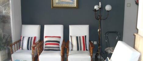Una sala de estar con tres sillones blancos, cada uno con un cojín a rayas, una mesa de centro de madera con revistas y un cuadro enmarcado en la pared.