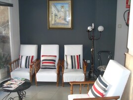 Una sala de estar con tres sillones blancos, cada uno con un cojín a rayas, una mesa de centro de madera con revistas y un cuadro enmarcado en la pared.