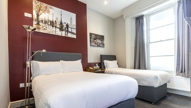 Een hotelkamer met twee bedden, een vloerlamp en kunstwerken aan de muur.