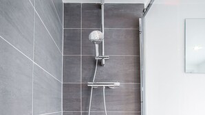 Een moderne douche met een handdouche en een slang, achter een wand van donkergrijze tegels.