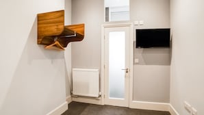 Een gang met een witte deur, een radiator, een houten decoratie en een tv aan de muur.