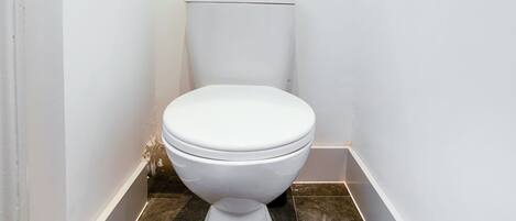 A small, clean bathroom with a white toilet, a mirror above it, and dark tiled flooring.