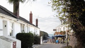 A narrow street lined with white terraced houses, a café with outdoor seating, and a cliffside in the background.