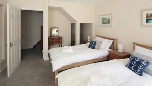 A hotel room with two single beds, a wooden nightstand, a dresser, a mirror, and a staircase leading to another level.