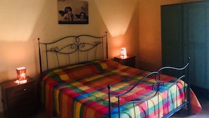 A bedroom with a metal bed frame, a colorful quilt, a bedside table with a lamp, and a green wardrobe. - Agriturismo Ilardo (Collesano)