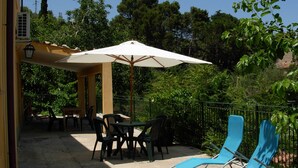 An outdoor patio with a table and chairs, a covered area with an umbrella, and two blue lounge chairs. - Agriturismo Ilardo (Collesano)