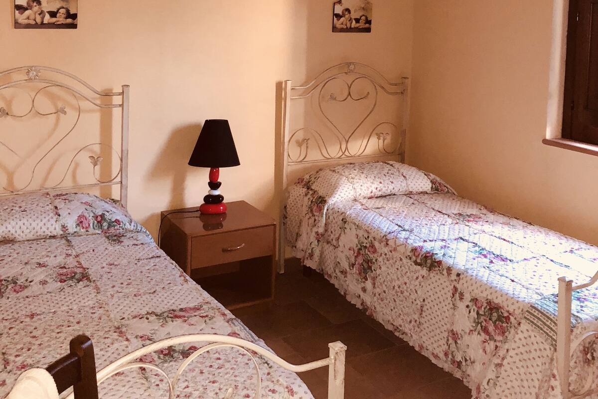 Un dormitorio con dos camas individuales, una mesita de noche con lámpara y dos cuadros en la pared.