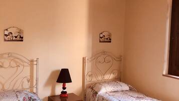 Una camera da letto con due letti singoli, un comodino con lampada e due quadri appesi al muro.