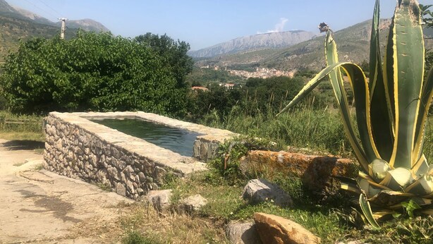 A stone structure with a small pool, surrounded by greenery and a view of a distant town and mountains. - Agriturismo Ilardo (Collesano)