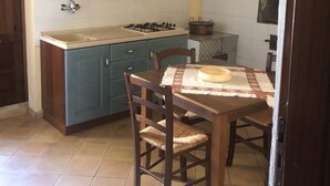 A compact kitchen with teal cabinets, a gas stove, and a dining table with chairs. - Agriturismo Ilardo (Collesano)