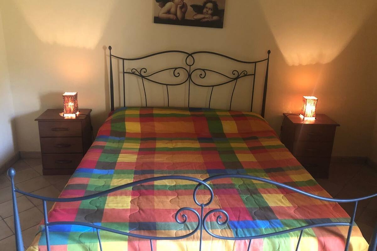 Una cama con un edredón de colores, dos mesitas de noche con lámparas y un cuadro en la pared.