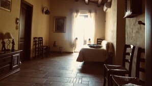 A room with a bed, wooden chairs, a small table, and a window with curtains. - Agriturismo Ilardo (Collesano)