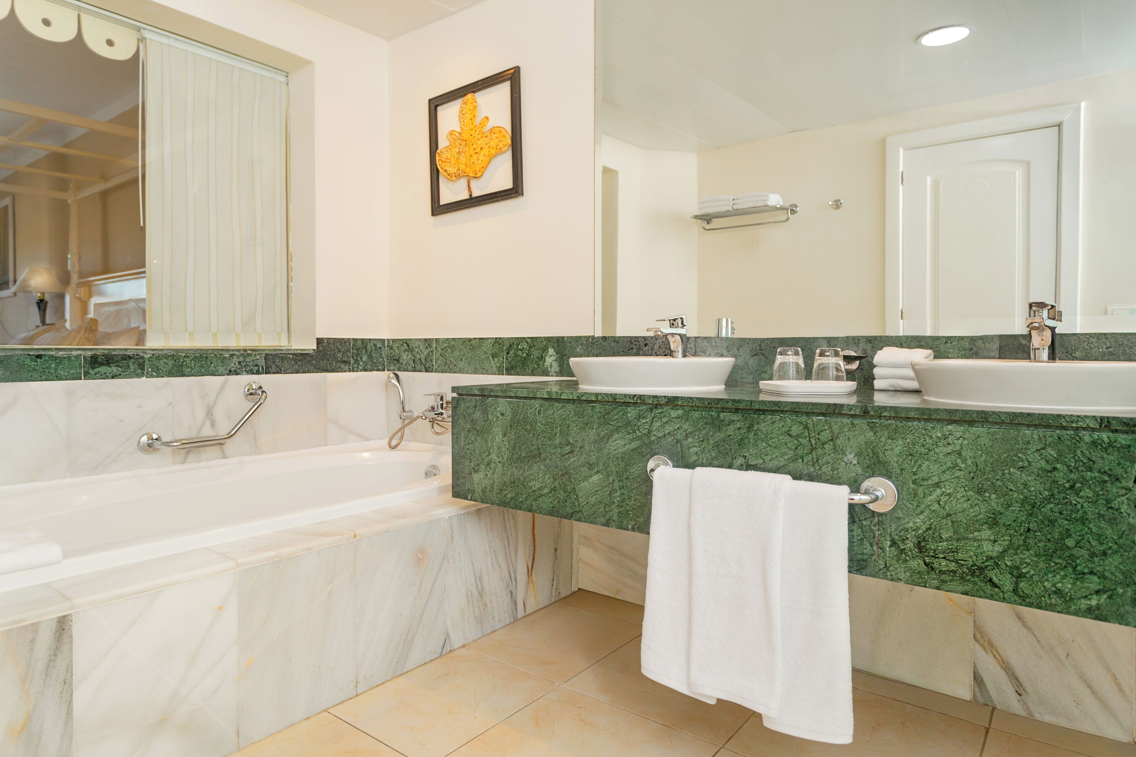 A bathroom with a bathtub, two sinks, a mirror, and a framed leaf decoration.
