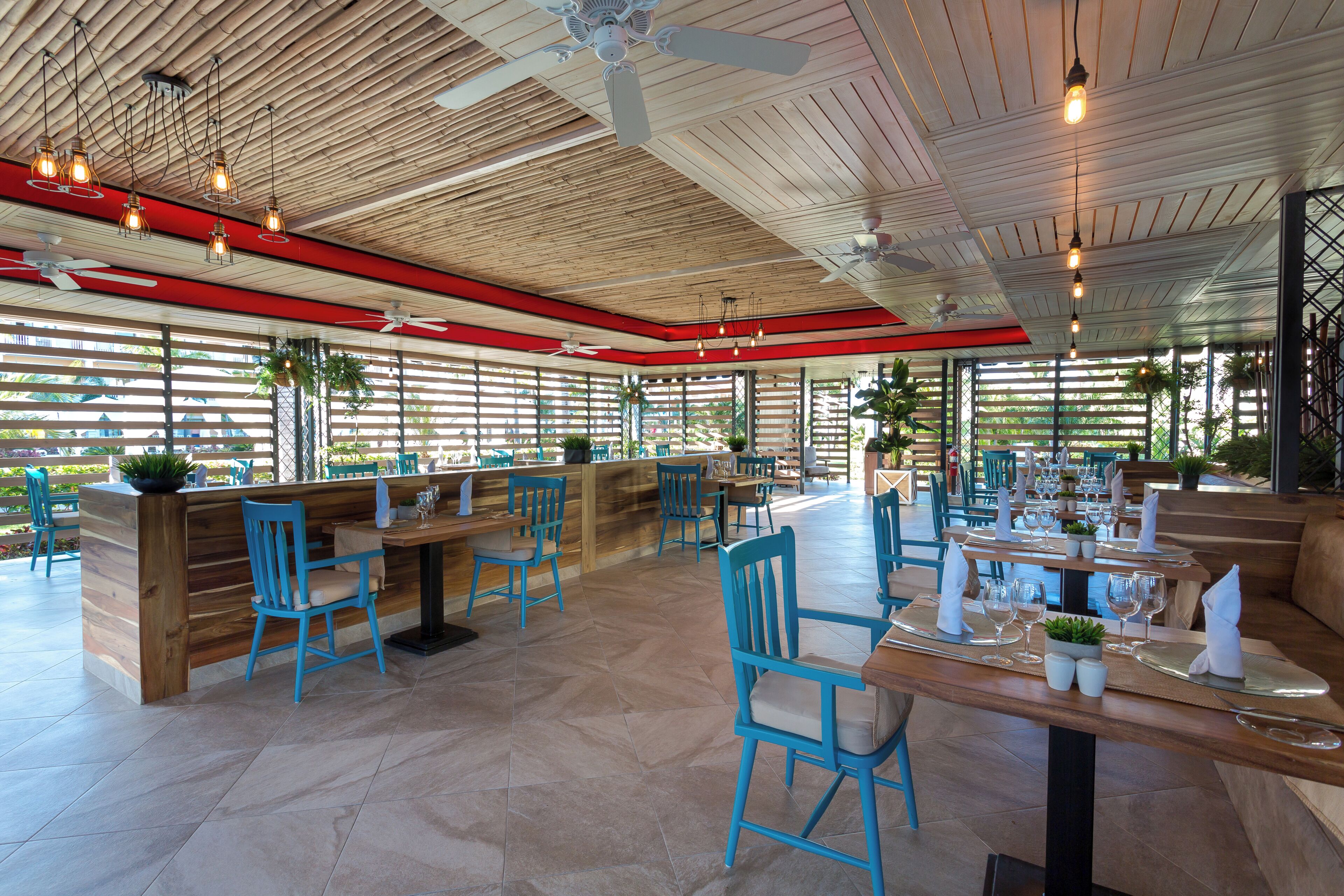 Ein Restaurant mit Holzbalkendecke, blauen Stühlen und gedeckten Tischen.