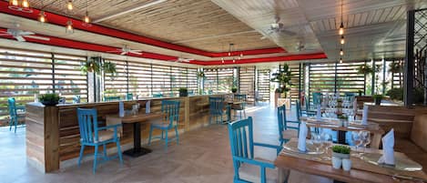 Ein Restaurant mit Holzbalkendecke, blauen Stühlen und gedeckten Tischen.
