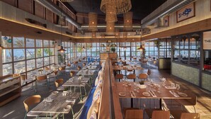 En rymlig restaurang med högt i tak, synliga ventilationskanaler och stora fönster med utsikt över staden.