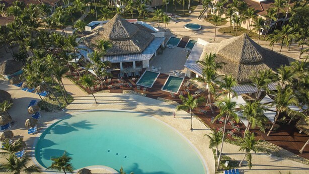 Ett semesterparadis med flera pooler, palmer och byggnader med halmtak.