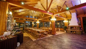 A spacious hall with wooden beams, large windows, and a fireplace. Tables are set for dining, and a Christmas tree is visible. - Eden Grand Resort (Predeal)