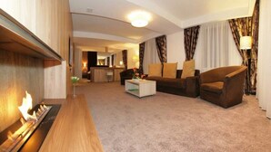 A modern hotel room with a living area featuring a sofa, armchairs, a coffee table, and a fireplace. - Eden Grand Resort (Predeal)