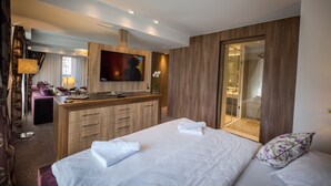 A modern hotel room with a large bed, a TV, a wooden desk, and a walk-in shower. - Eden Grand Resort (Predeal)