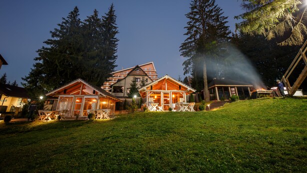 A lodge with multiple wooden cabins, a dining area, and a large building with a glass facade. - Eden Grand Resort (Predeal)