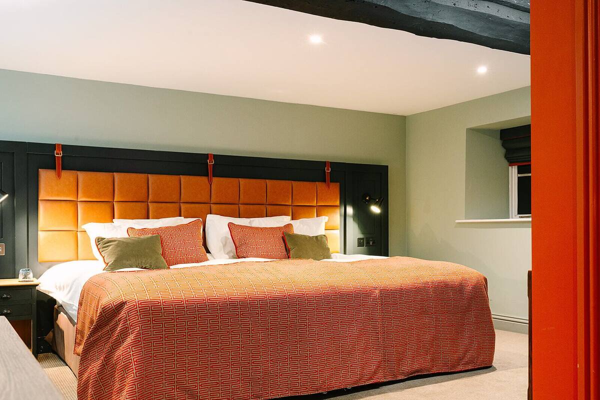 A modern bedroom with a large bed, a headboard with a leather panel, and a bedside table with a lamp.