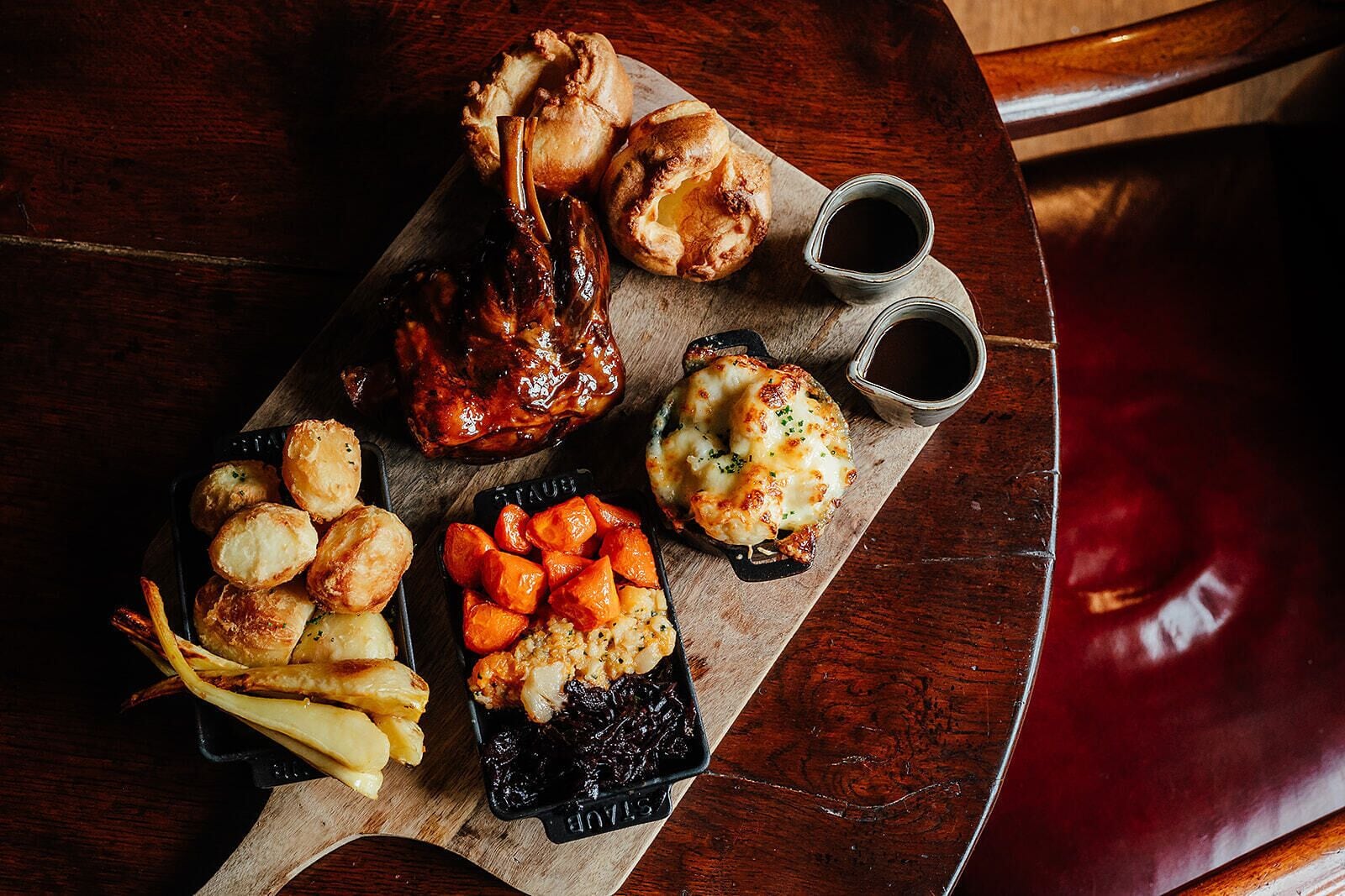 A wooden table with a variety of dishes including roasted meat, potatoes, and vegetables.
