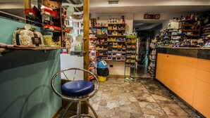 A narrow corridor with shelves stocked with various items, a blue chair, and a trash bin. - Hotel la Spagnola (Amantea)