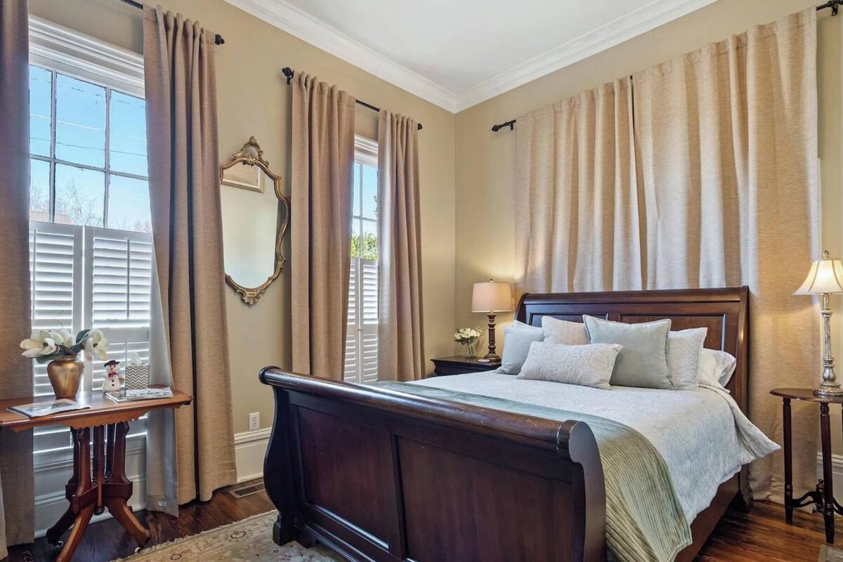 A bedroom with a large bed, a bedside table, a mirror, and a window with curtains.