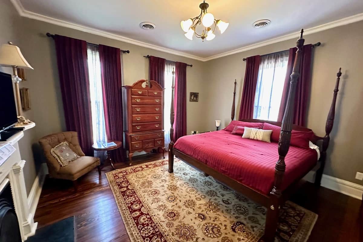 A bedroom with a four-poster bed, a wooden dresser, a chair, and a television on a stand.