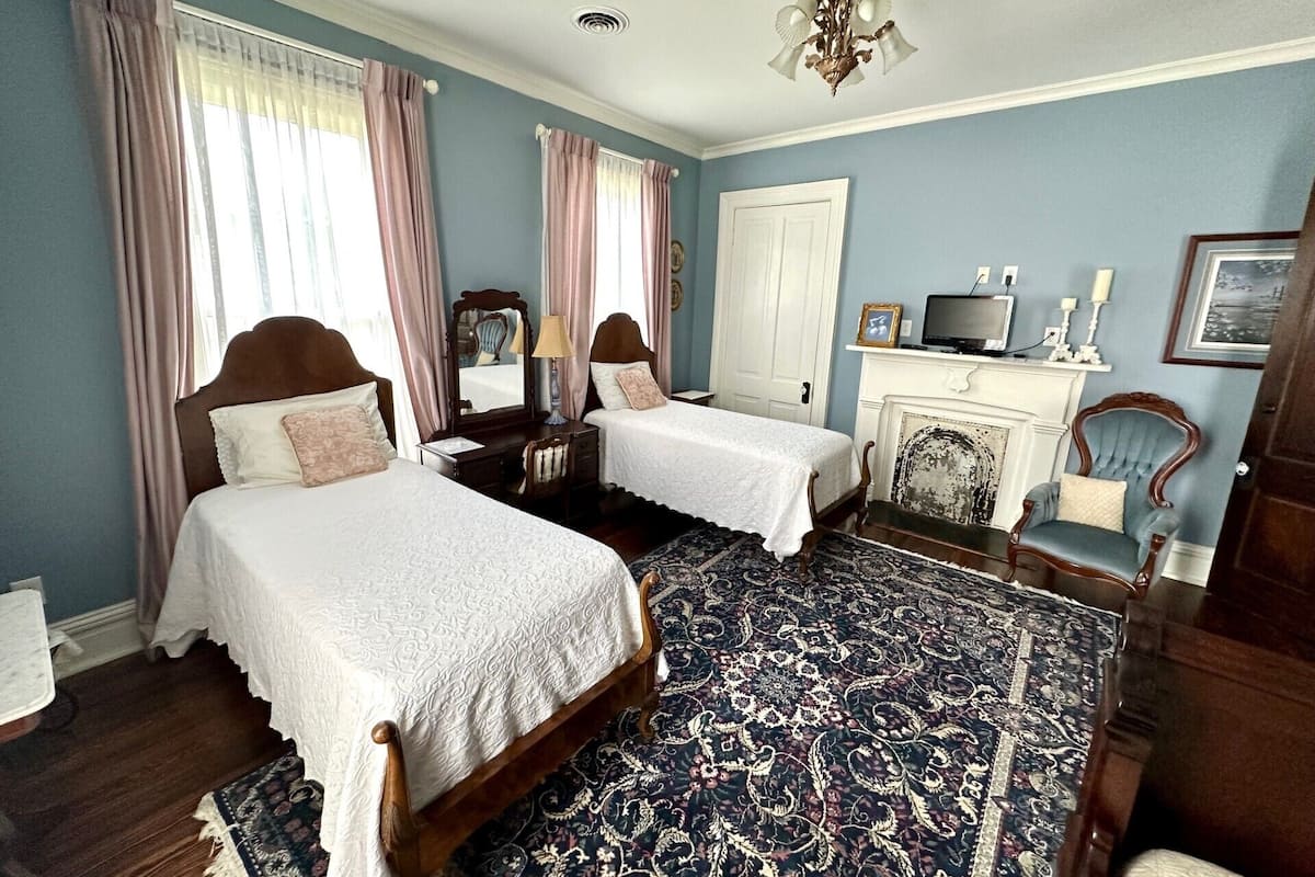 A bedroom with two beds, a chandelier, a fireplace, and a chair.